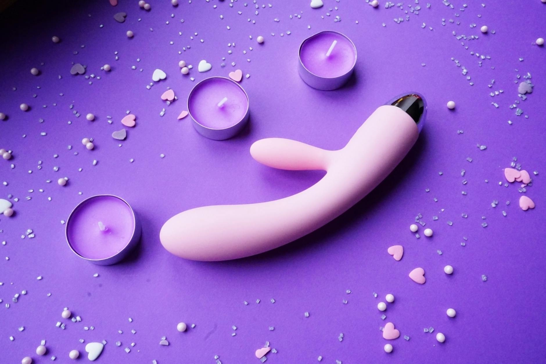Pink vibrator on a purple background surrounded by heart confetti and candles for romantic atmosphere